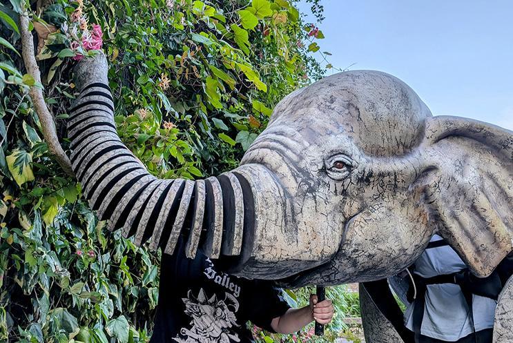A puppet elephant picking flowers from a hedge