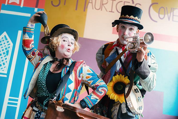 Two performers dressed as clowns playing instruments in front of a colourful wall.