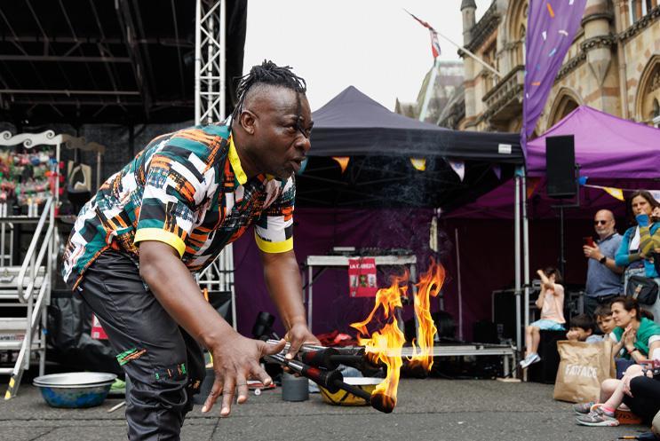 A performer talking to the audience with fire sticks in his hands.