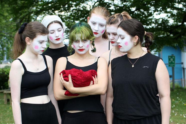 A group of young woman in clown face paint, holding a baby
