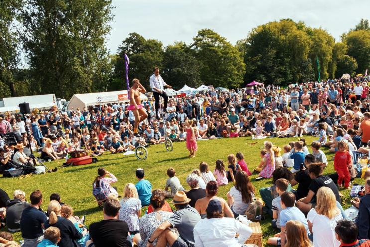 Large crowd of people sitting in a circle watching performers who are on unicycles and juggling fire 